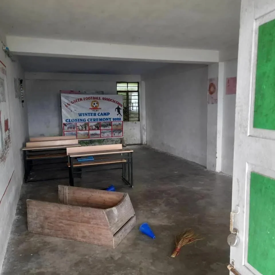 A collection of books sits on a table beside classroom boards.