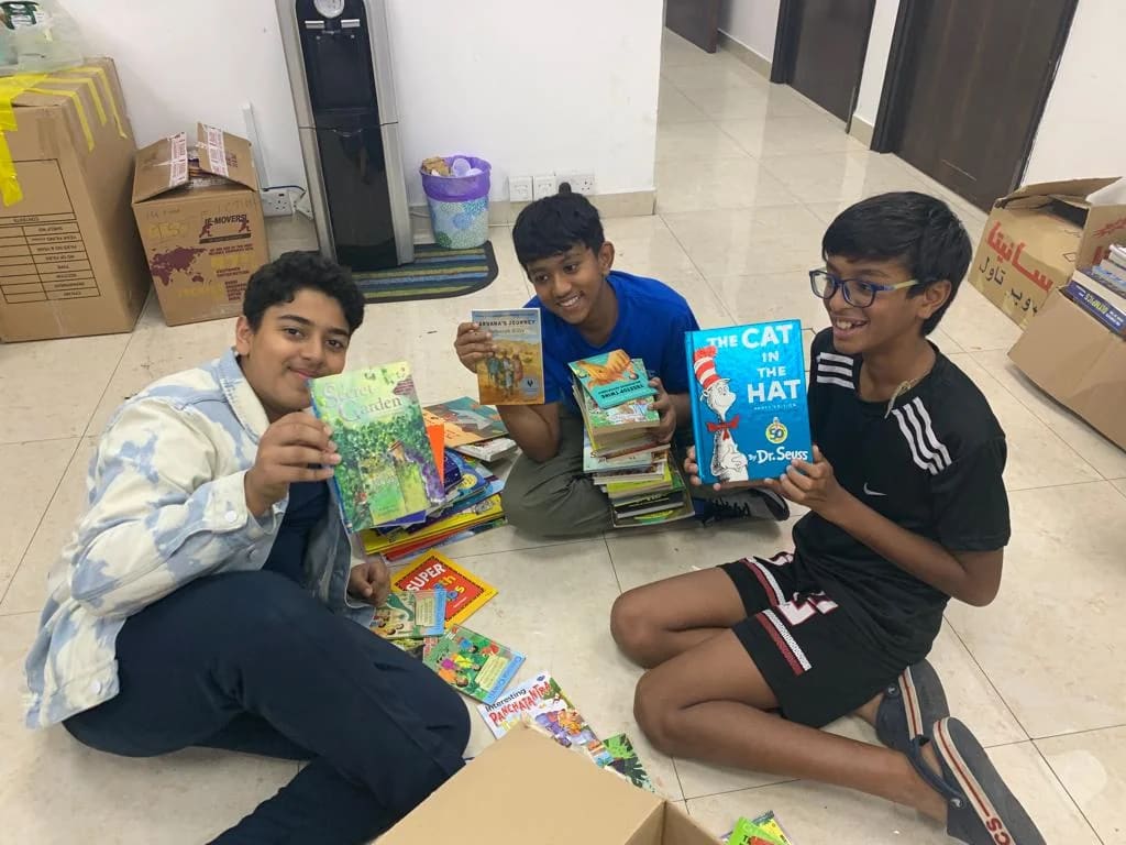 Three young volunteers sort and hold books during a collection drive.