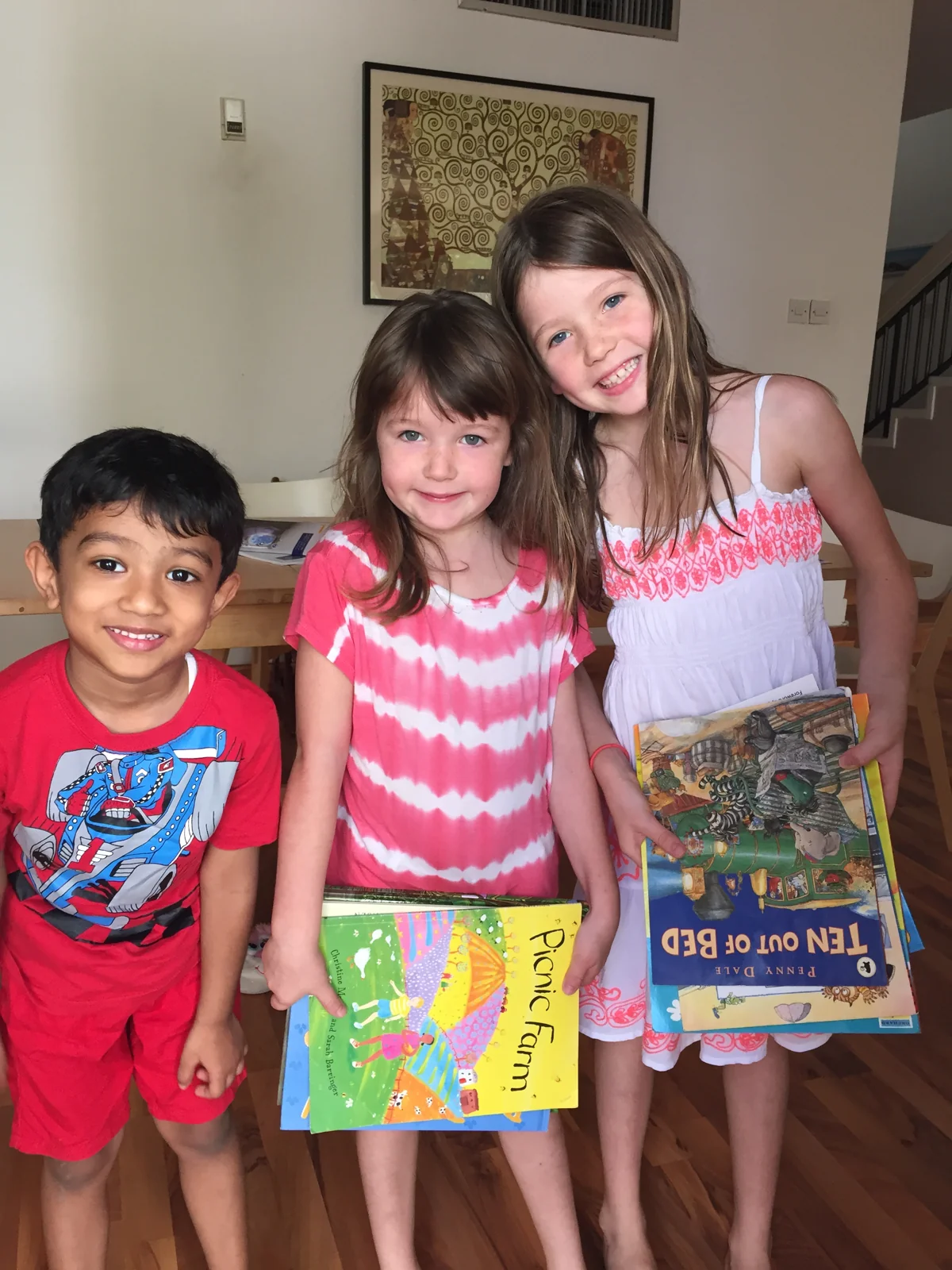 Three young children hold their books at a neighbourhood collection.