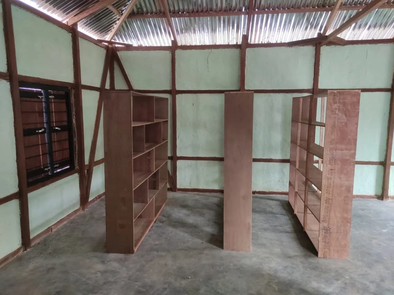 An empty room in Manipur with newly built wooden shelves standing on a bare concrete floor